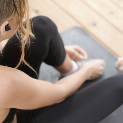 woman in workout gear, sits on a yoga mat and ties her shoe
